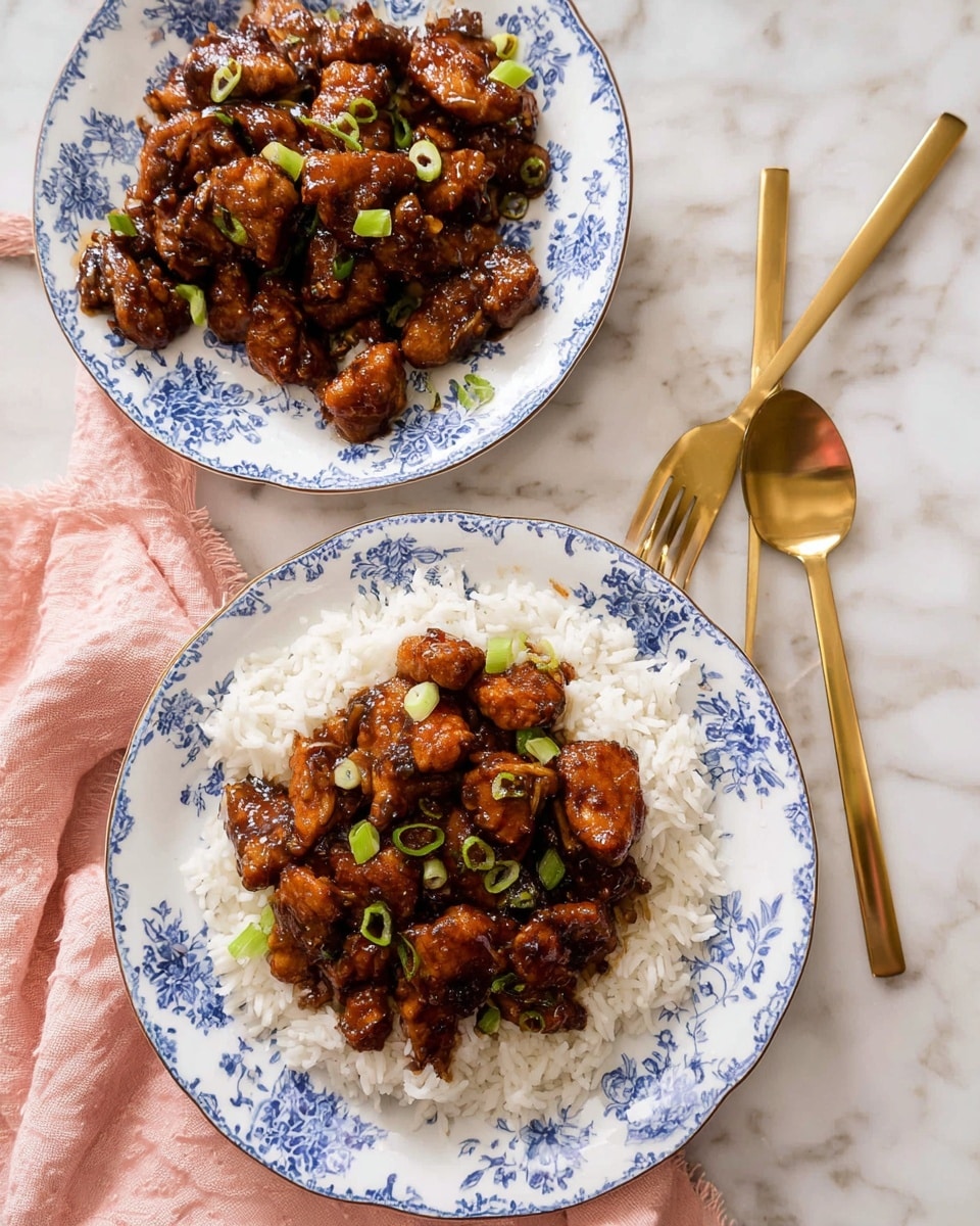 The image shows a serving of dark brown glazed chicken pieces on top of a white bed of rice, all placed on a white plate with a blue floral pattern. The chicken pieces are shiny and slightly sticky, sprinkled with small green onion slices. Behind this plate, there is an oval white dish with the same blue floral pattern, filled with more glazed chicken pieces. The setting is on a white marbled surface, accompanied by a light pink cloth on the left side and gold-colored fork near the cloth. On the right side, there are two gold-colored serving spoons. photo taken with an iphone --ar 4:5 --v 7