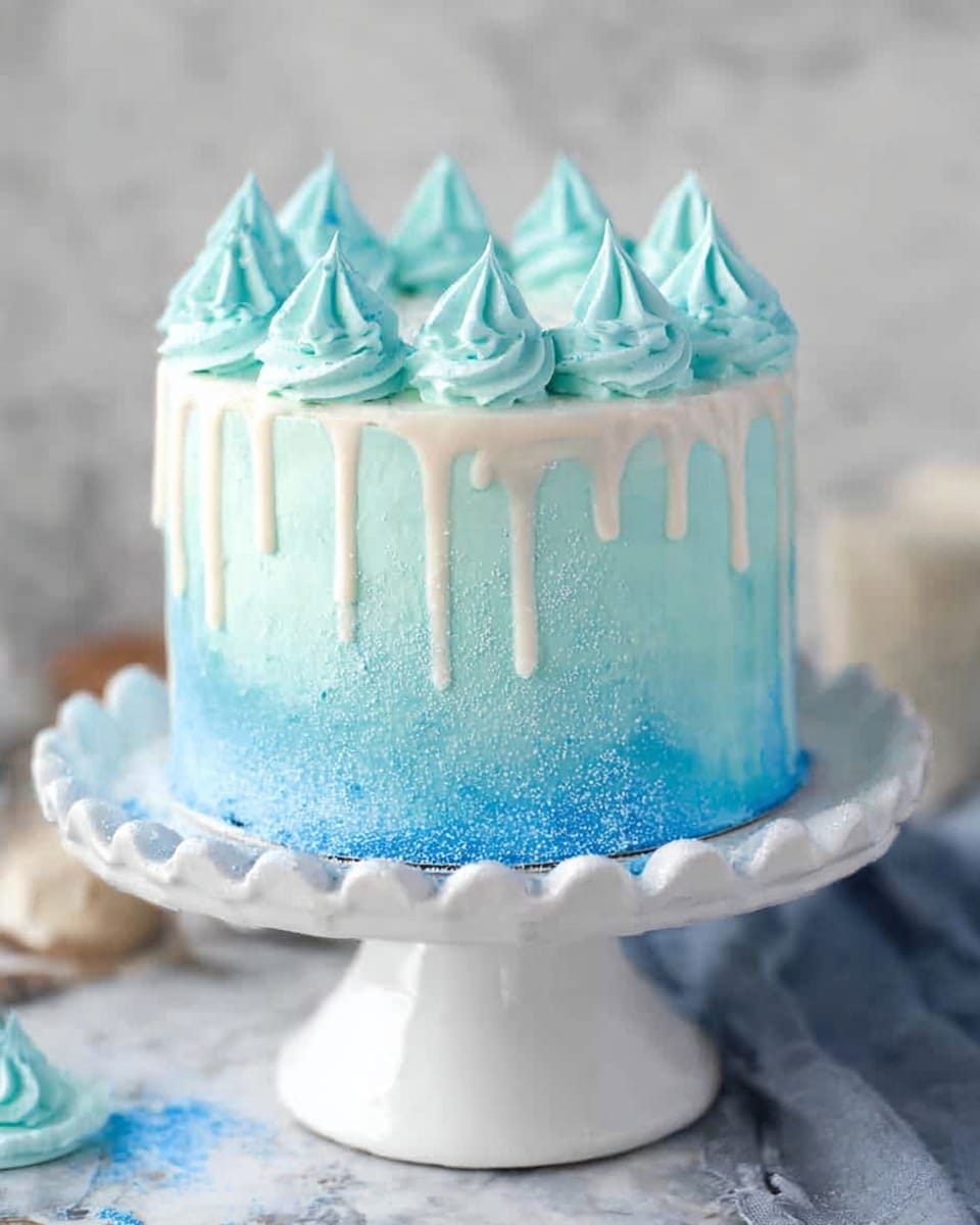A tall, round cake with smooth white frosting gradually changing into bright blue sugar crystals from top to bottom, creating a sparkling ombre effect. The cake is topped with a ring of evenly spaced white dollops of frosting, each dipped in blue sugar on the lower half, forming pointed peaks. It sits on a simple white cake stand against a white marbled surface with soft bokeh lights in the background, giving a festive and elegant look. photo taken with an iphone --ar 4:5 --v 7