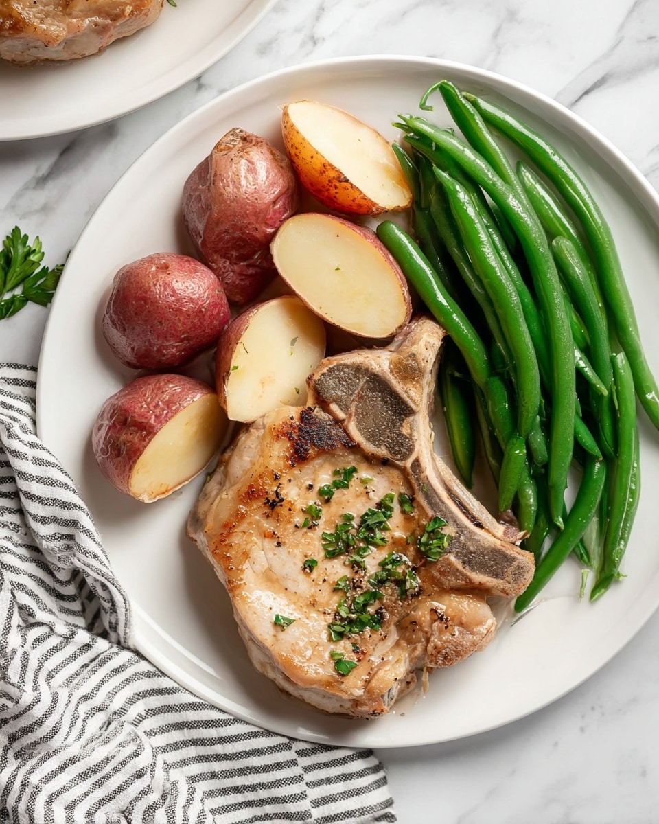 The dish is on a white plate placed on a white marbled surface with a black and white striped cloth nearby. On the plate, there is one large, lightly browned pork chop positioned on the bottom right, showing a slightly crispy texture with some herbs sprinkled on top. To the left of the pork chop, there are several red-skinned potatoes cut into chunks with soft yellow insides visible. On the top right of the plate, there is a neat pile of bright green cooked green beans, with their smooth texture intact. The dish is simple, clean, and nicely arranged. photo taken with an iphone --ar 4:5 --v 7