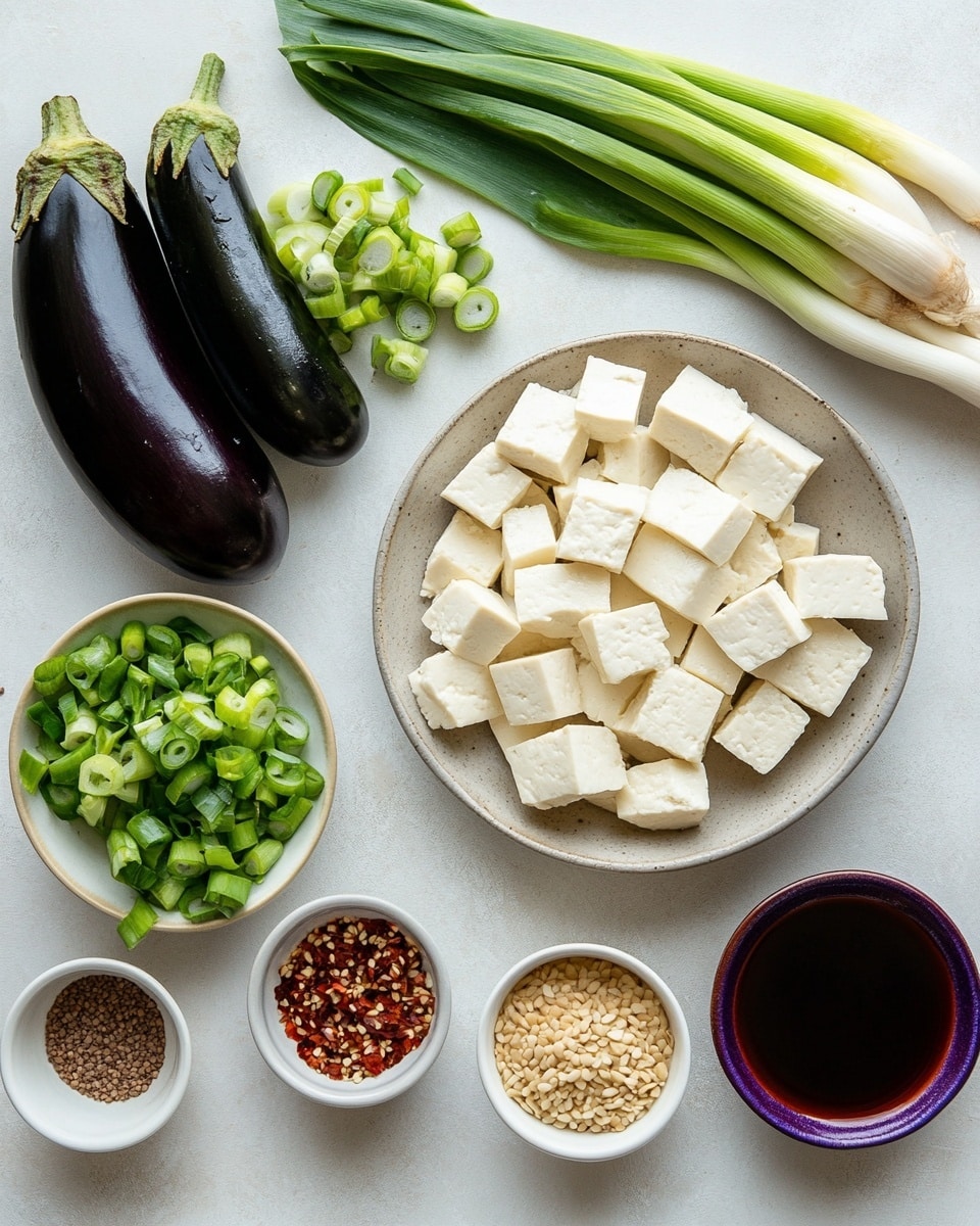A close-up view of a silver pan filled with a spicy stew that has several layers. The bottom layer is a dark red-brown broth with visible oil and small bits of spices. Floating in the broth are several white tofu chunks with smooth texture, some showing small red chili pieces on top. Long dark purple eggplants are scattered throughout, partially submerged in the broth, their skins glossy and soft. Small green pieces of chopped scallions float on top, adding a fresh color contrast. The pan handle extends out to the right, and the whole scene sits on a black stove, with a white marbled texture in the background. Photo taken with an iphone --ar 4:5 --v 7